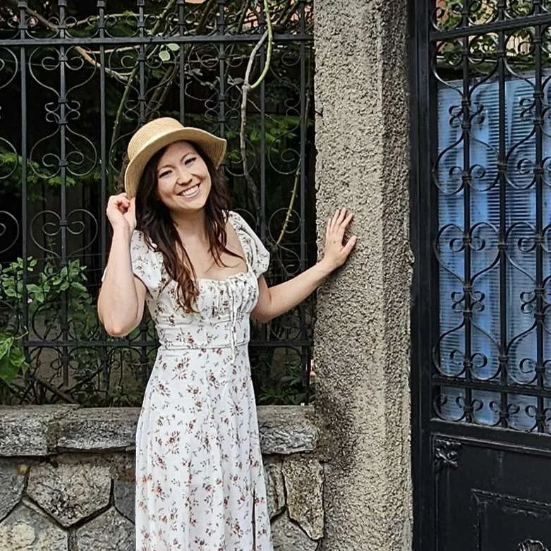 Woman in a white dress and wearing a hat standing in front of a door fence with roses in Korca Albania